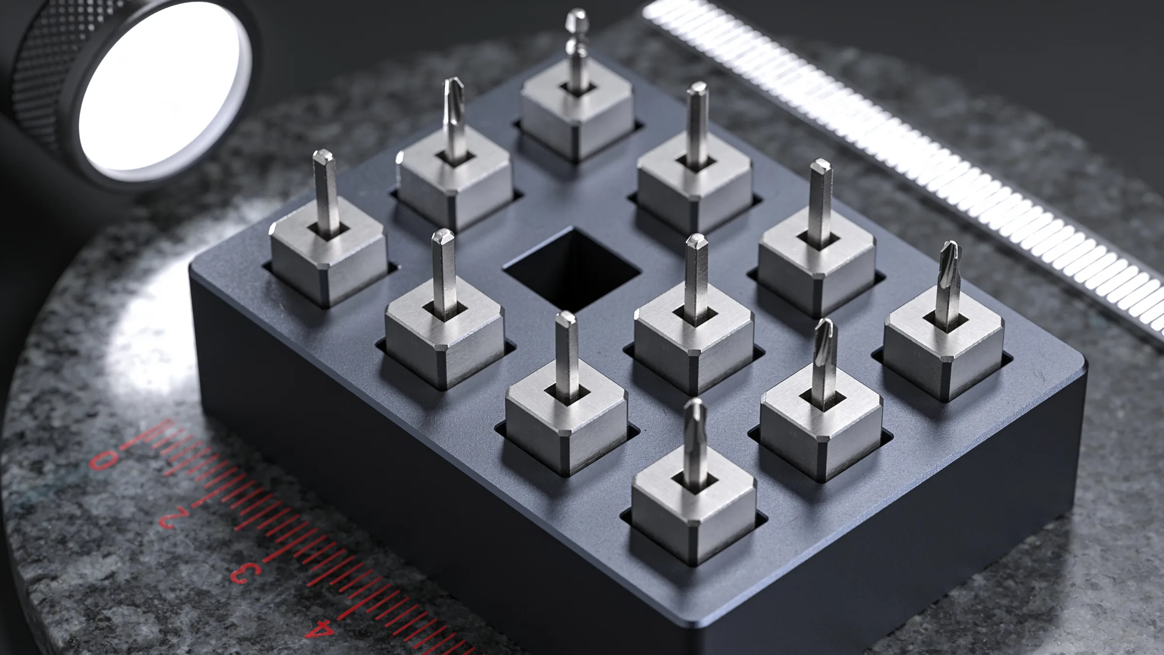 Machined steel keys seated in a dark anodized holder block under an inspection lamp, with one slot in the middle of the block left empty.